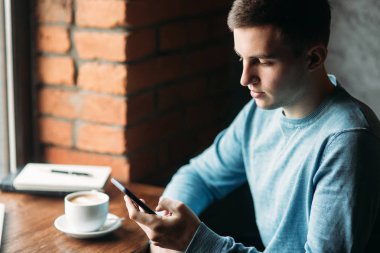 Adam bir kafede telefonuyla pencerenin oturuyor. Evet