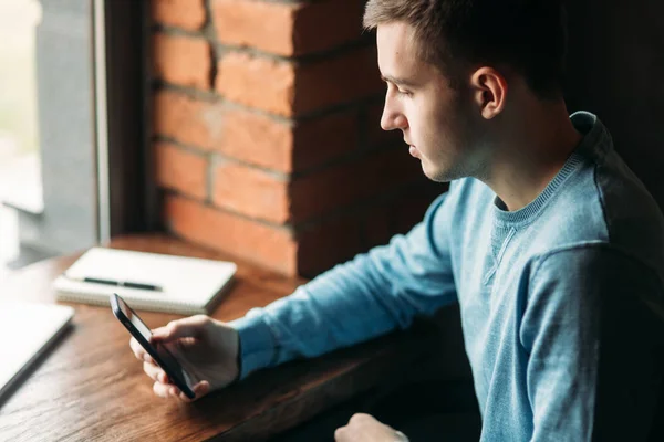 Man med telefonen på ett café sitter mittemot fönstret — Stockfoto