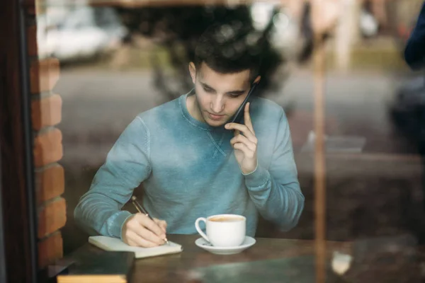 Man med telefonen på ett café sitter mittemot fönstret. Prata i telefon. Visa från fönstret — Stockfoto