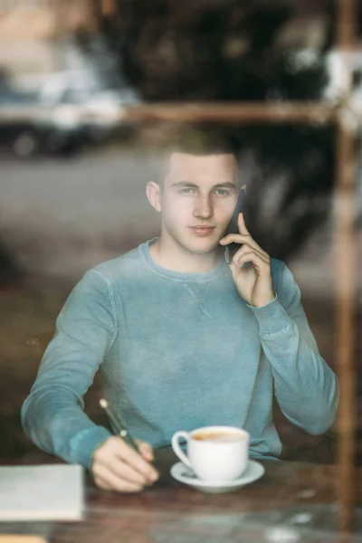 Ein Mann mit Telefon in einem Café sitzt dem Fenster gegenüber. telefonieren. Blick aus dem Fenster — Stockfoto