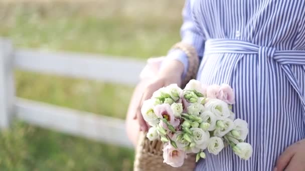 Close up view of pregnant belly in nature. Woman hold bouquet and caress her belly — Stock Video