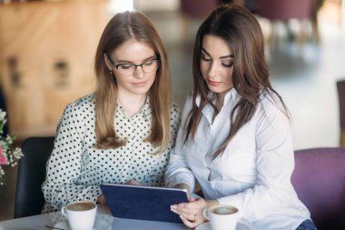 İki kız bir tablet bir kafede oturan ve kahve içme kullanma