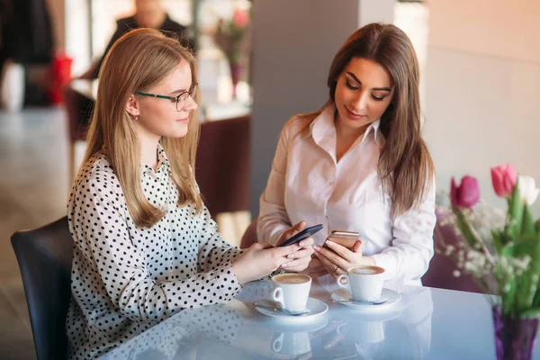 Mädchen sitzen in einem Café, trinken Cappuccino und telefonieren — Stockfoto