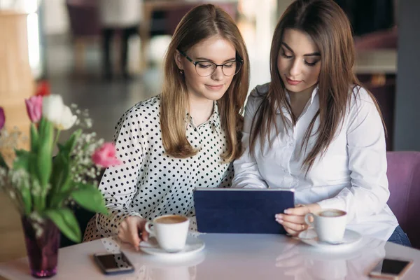 Zwei Mädchen benutzen ein Tablet, während sie in einem Café sitzen und Kaffee trinken — Stockfoto
