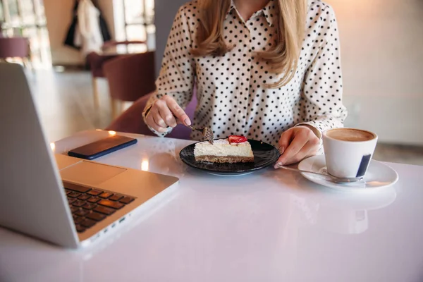 Mädchen beim Kuchenessen in einem Café. Blondine im gepunkteten Hemd mit Laptop — Stockfoto
