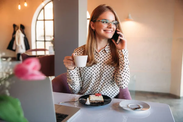 Mädchen beim Kuchenessen in einem Café. Blondine im gepunkteten Hemd mit Laptop — Stockfoto