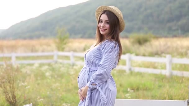 Mujer embarazada en vestido azul y sombrero de punto posa a la cámara — Vídeos de Stock