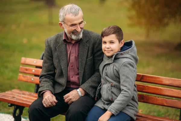 爷爷和他的孙子一起在公园里消磨时间。他们坐在长凳上。 — 图库照片