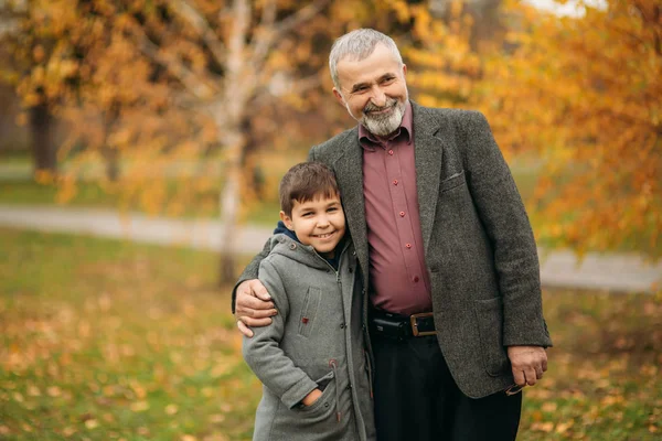 Grandpa and grandson spend time in autumn park. They hug each other and walk. Fmily time