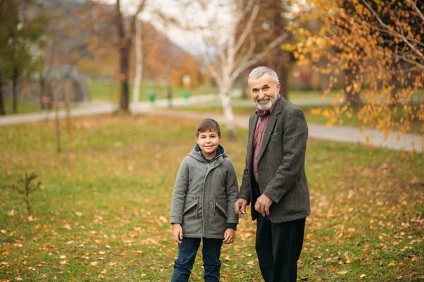 Grandpa and grandson spend time in autumn park. They hug each other and walk. Fmily time