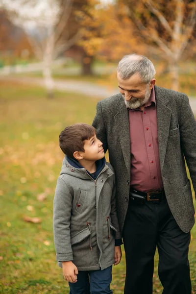 爷爷和孙子花时间在秋季公园。他们互相拥抱, 走路。着眼点时间 — 图库照片