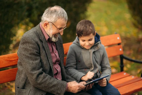 Kleinzoon hoe zijn grootvader tablet gebruiken. Kind helpen oudere generatie — Stockfoto