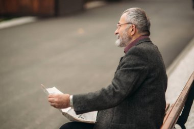 Gri ceketli güzel sakallı yakışıklı dedesi parkta bir bankta oturur ve bir gazete okuyor