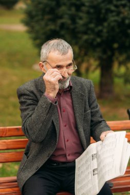 Gri ceketli güzel sakallı yakışıklı dedesi parkta bir bankta oturur ve bir gazete okuyor