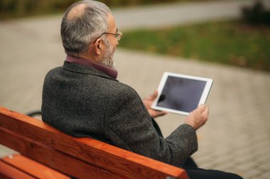 Büyükbaba bir tablet kullanır ve parkta bankta oturur. O video izle