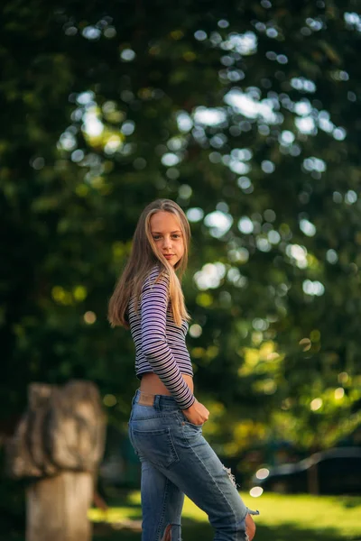 Блондинка-подросток в полосатой блузке на фоне зеленого дерева — стоковое фото