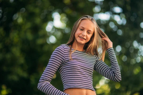 Blondes Teenager-Mädchen in gestreifter Bluse auf dem Hintergrund eines grünen Baumes — Stockfoto