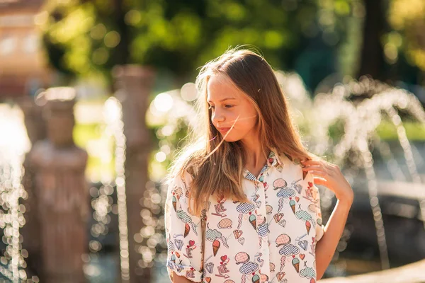 Blond dospívající dívka v blond halenku, hrát si s vlasy na pozadí fontány — Stock fotografie