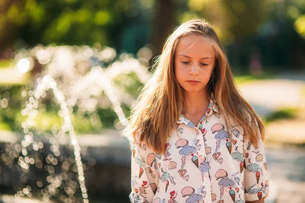 Blond teenage girl in a blond blouse playing with her hair on the background of a fountain — Stock Photo, Image