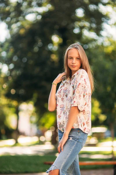 Blond meisje in blouse poseren voor de fotograaf tegen de achtergrond van de groene boom — Stockfoto