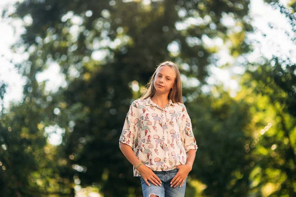 Blondes Mädchen in Bluse posiert vor dem Hintergrund eines grünen Baumes für Fotografen — Stockfoto