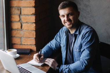 Bir sakallı bir kafede bir dizüstü bilgisayar kullanır ve bir Not yazar