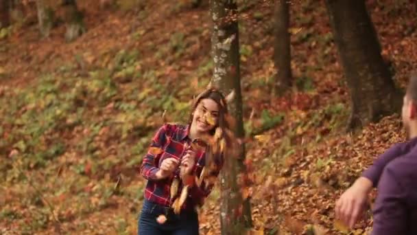 Giovane ragazza giocare con ragazzo utilizza foglie nel parco autunnale — Video Stock