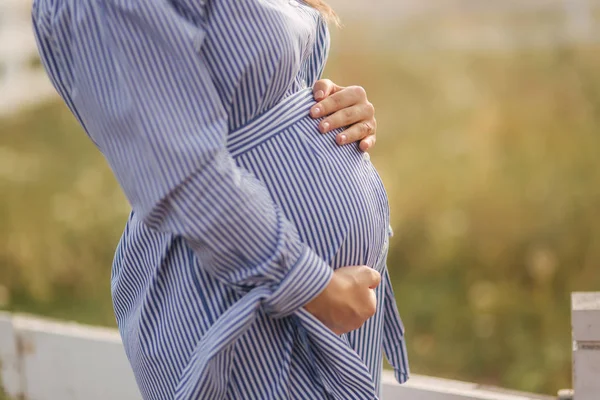 Крупный план беременного живота в природе. Женщина держит букет и ласкает живот — стоковое фото