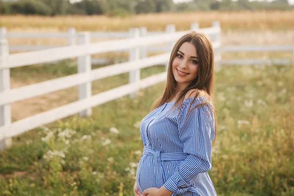 近观美丽的孕妇在蓝色礼服散步听到农场。微笑和幸福 — 图库照片