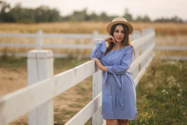 Une femme enceinte coiffée d'un chapeau se tient près de la barrière. ferme. Contexte du domaine — Photo