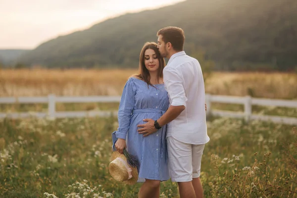 Ma und seine schwangere frau stehen auf einem feld in der nähe des bauernhofs und umarmen sich — Stockfoto