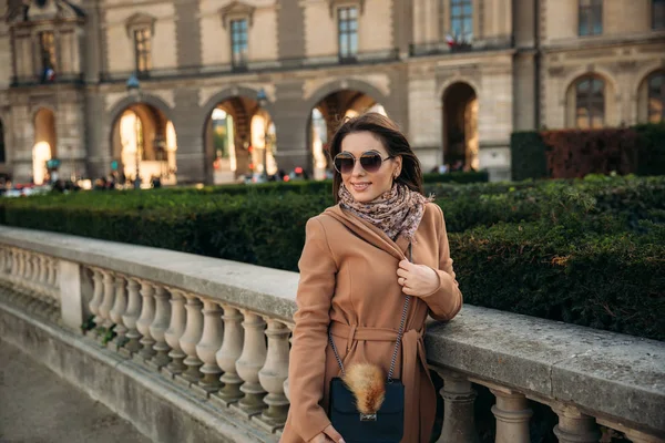 Menina elegante no casaco posando para fotógrafo perto do grande parque. tempo ensolarado e modelo bonito — Fotografia de Stock