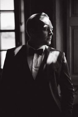 Yakışıklı adam uygun ve yay stand pencerenin kravat. Siyah beyaz resim