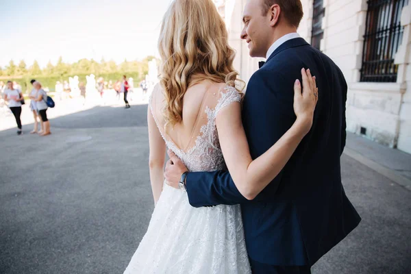 Caminhada de casal perto do grande palácio. Elegante noivo e noiva em suas roupas de casamento. Amor. — Fotografia de Stock