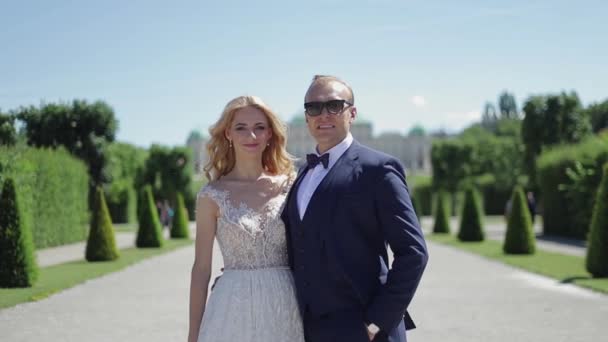 Couple walk near the big palace. Elegant groom and bride in their wedding clothes. Love — Stock Video