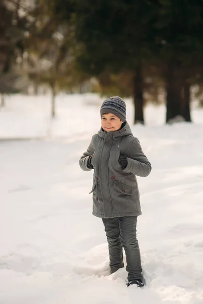 Um garotinho caminha no parque no inverno, joga bolas de neve e se alegra. À espera de clima de Natal — Fotografia de Stock