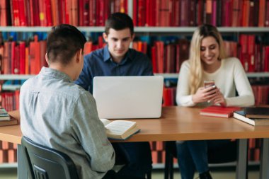 Üniversite öğrencileri kitap ve dizüstü bilgisayar ile birlikte masada oturuyor. Mutlu genç insanlar Kitaplığı'nda grup çalışması yapıyor