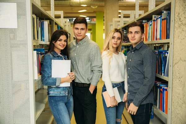 Grupo de estudiantes quieren encontrar un poco de literatura útil para la preparación para el examen universitario. Dos chicos y dos chicas — Foto de Stock