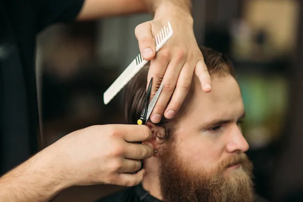 Barbeiro usando tesoura e pente na barbearia — Fotografia de Stock