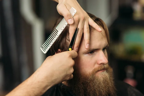 Las manos de joven peluquero haciendo corte de pelo a hombre barbudo atractivo en la barbería — Foto de Stock