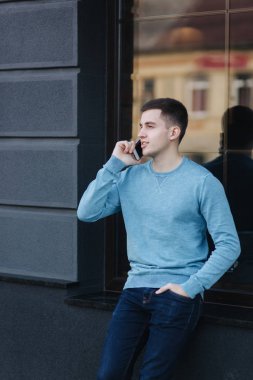 Yakışıklı adam sokakta telefonu kullanıyor. Telefonda konuşurken. Kazaklı genç adam