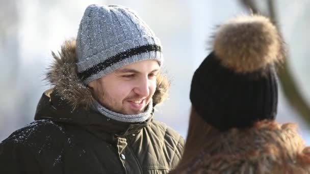 Un chico joven y una chica vestida con ropa de invierno cálido, disfrutar de la presencia de los demás en un parque de invierno nevado — Vídeos de Stock