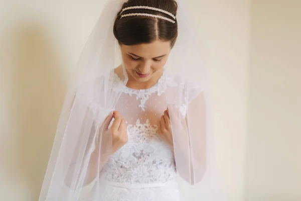 Krásná nevěsta stát poblíž okna v bílých svatebních šatech. Šarmantní dáma — Stock fotografie