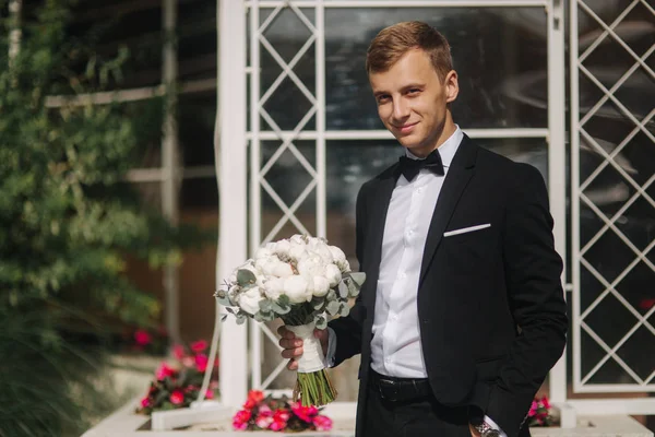 Щасливий наречений у стильному костюмі бере букет наречених і посміхається — стокове фото