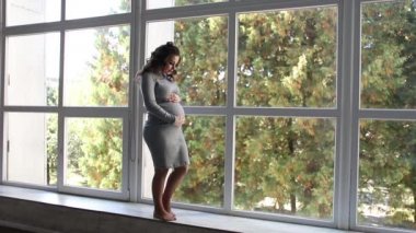 Hamile kadın güzel gri elbiseli pencerenin duran ve karnı okşayarak