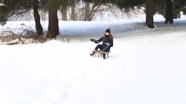 Vacker flicka i svarta kläder rida på en snöig berg av släden. Kälkåkning — Stockvideo