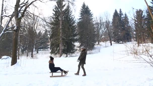 Jongen en meisje rodelen. Besneeuwde winterweer. Gelukkige familie. Kerstsfeer. Man helpt meisje rodelen — Stockvideo