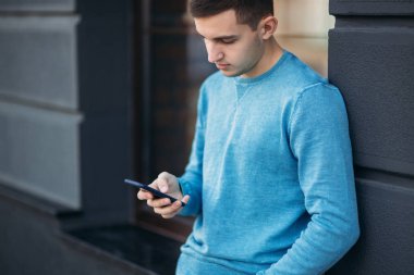 Genç adam sokakta telefonu kullanıyor. Yakışıklı olan pencerenin önünde stand