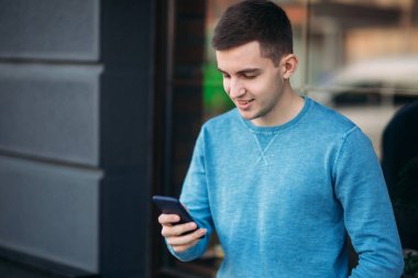 Genç adam sokakta telefonu kullanıyor. Yakışıklı olan pencerenin önünde stand