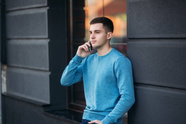 Yakışıklı adam sokakta telefonu kullanıyor. Telefonda konuşurken. Kazaklı genç adam